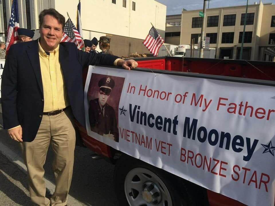 Alex posing with a banner honoring his veteran father.